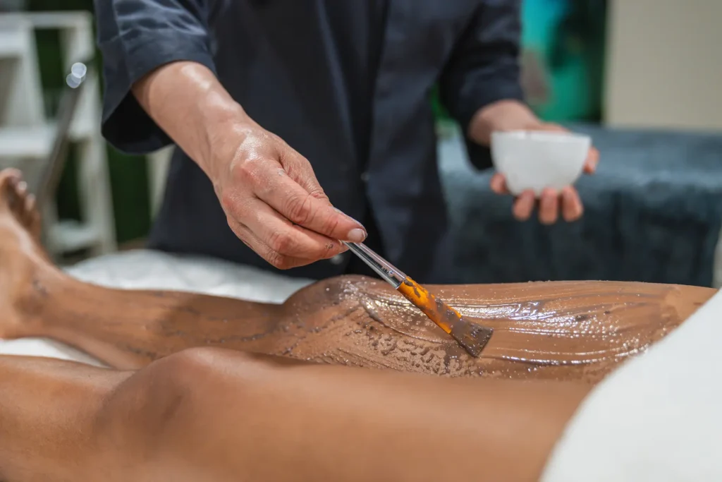 beautician applying chocolate cream on woman s leg 2025 05 20 19 21 11 utc